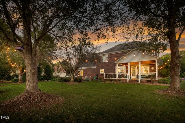 back house at dusk with a lawn and a porch