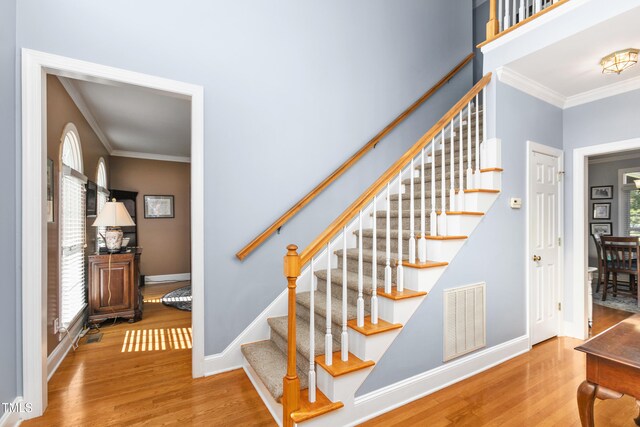 stairway with ornamental molding and hardwood / wood-style floors