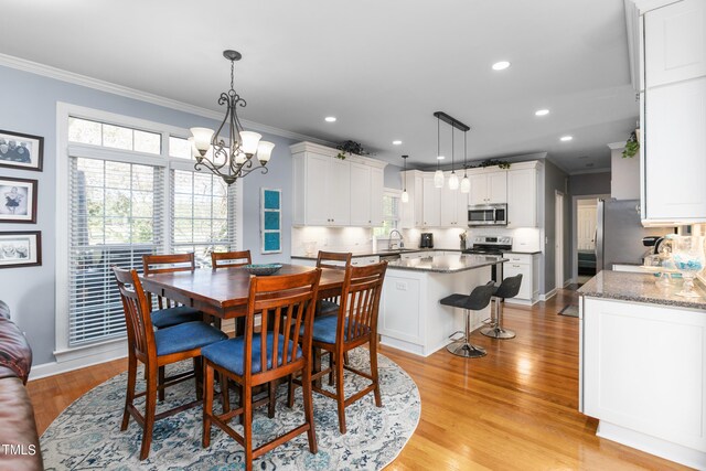 dining area with a chandelier, ornamental molding, sink, and light wood-type flooring