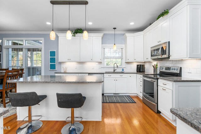 kitchen with appliances with stainless steel finishes, sink, a kitchen breakfast bar, white cabinetry, and hanging light fixtures