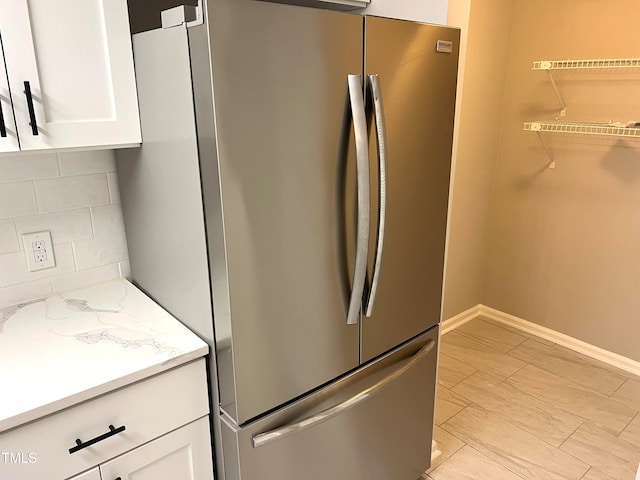 kitchen featuring light stone counters, backsplash, stainless steel fridge, and white cabinetry