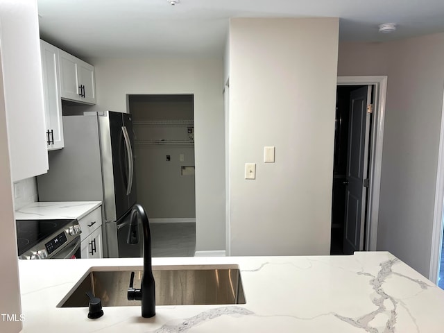 kitchen featuring light stone countertops, stainless steel electric range oven, sink, and white cabinets