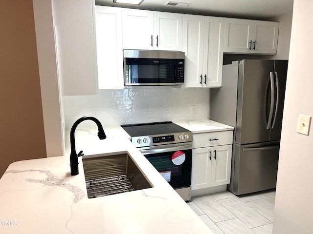 kitchen with appliances with stainless steel finishes, light stone counters, backsplash, and white cabinets