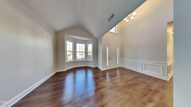 interior space featuring wood-type flooring, a notable chandelier, vaulted ceiling, and a textured ceiling