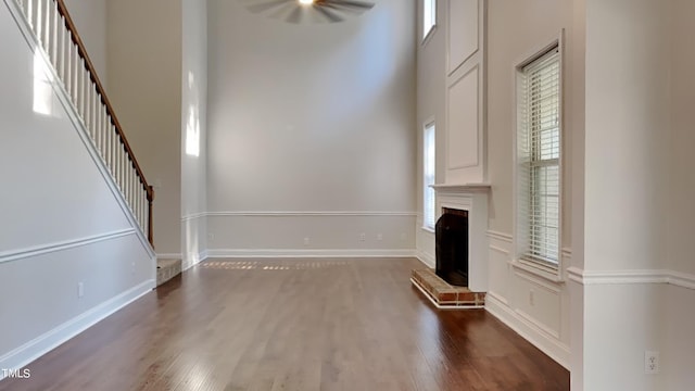 unfurnished living room with a brick fireplace, a towering ceiling, and dark hardwood / wood-style floors