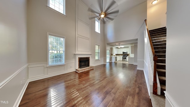 unfurnished living room featuring a fireplace, a towering ceiling, dark wood-type flooring, and plenty of natural light