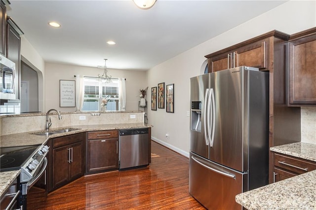 kitchen featuring light stone counters, stainless steel appliances, hanging light fixtures, and dark wood-type flooring