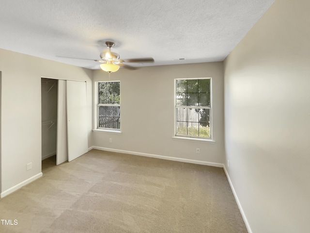 unfurnished bedroom featuring a textured ceiling, light colored carpet, multiple windows, and ceiling fan