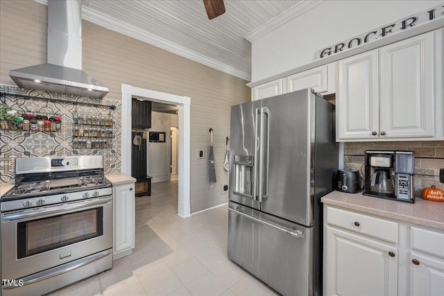 kitchen with ceiling fan, white cabinets, ornamental molding, wall chimney range hood, and stainless steel appliances