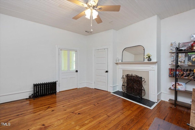 unfurnished living room with hardwood / wood-style floors, ceiling fan, and radiator heating unit