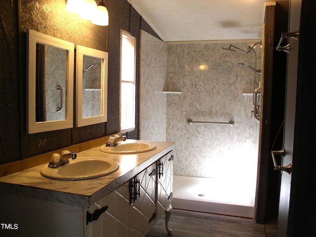 bathroom featuring a textured ceiling, hardwood / wood-style floors, vaulted ceiling, tiled shower, and vanity