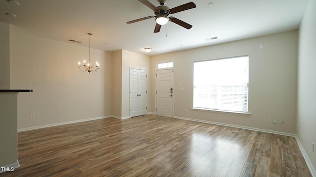 empty room featuring wood finished floors, visible vents, baseboards, and ceiling fan with notable chandelier