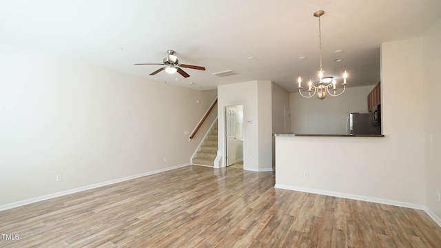 unfurnished living room featuring visible vents, stairs, light wood-type flooring, and ceiling fan with notable chandelier