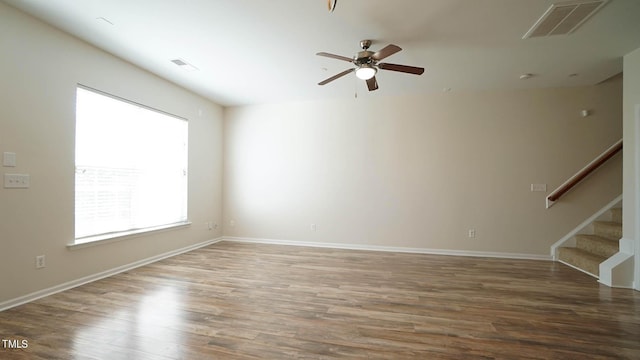 spare room featuring a ceiling fan, stairs, wood finished floors, baseboards, and visible vents