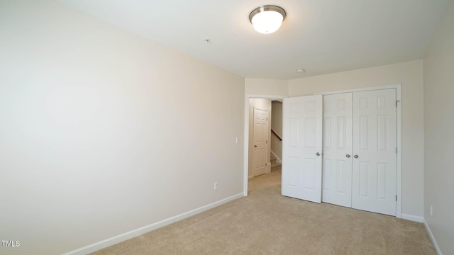 unfurnished bedroom featuring light colored carpet, baseboards, and a closet