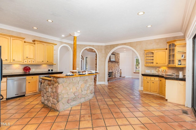 kitchen with decorative backsplash, stainless steel dishwasher, ornamental molding, a center island, and a stone fireplace