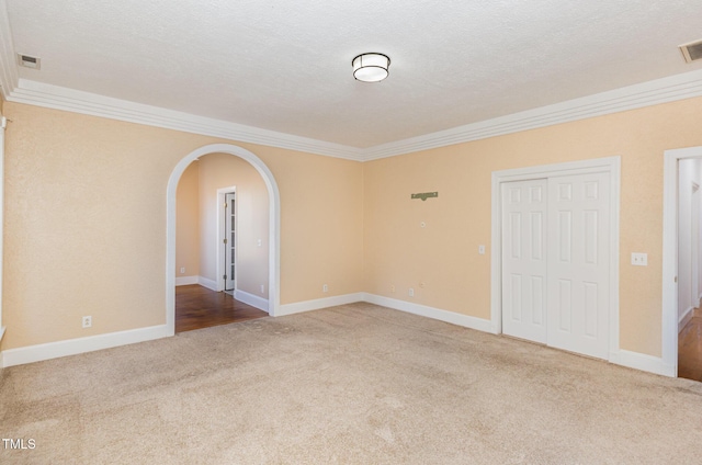 empty room featuring a textured ceiling, light colored carpet, and crown molding