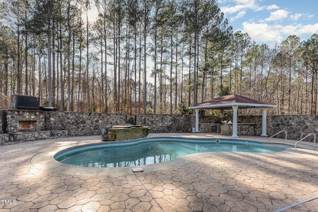 view of pool with a gazebo, an outdoor stone fireplace, and a patio area