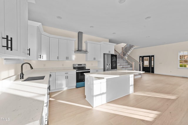 kitchen featuring appliances with stainless steel finishes, wall chimney exhaust hood, sink, white cabinets, and a center island