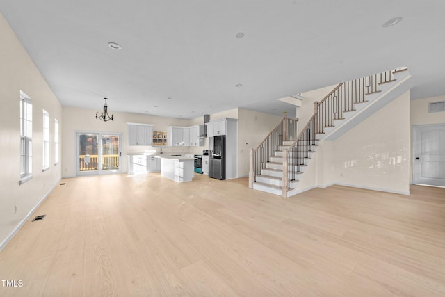 unfurnished living room with light wood-type flooring and an inviting chandelier