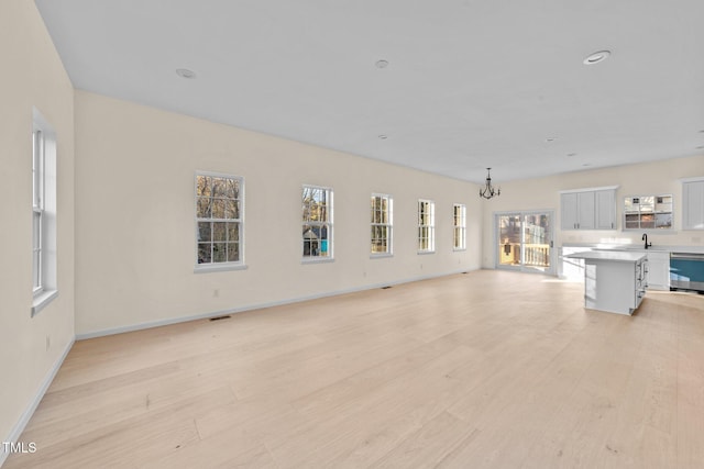 unfurnished living room featuring light wood-type flooring, a notable chandelier, and sink