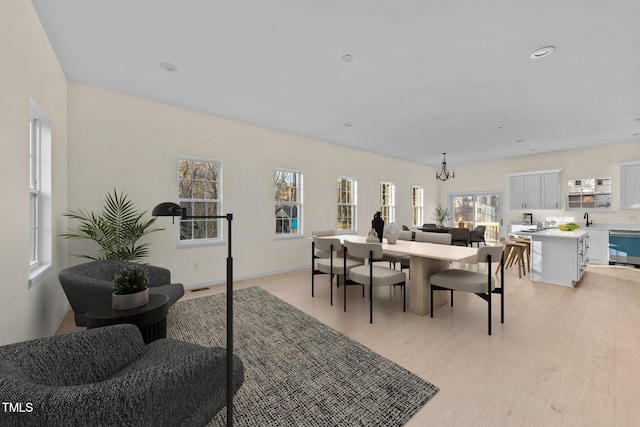 dining space featuring light wood-type flooring, sink, a wealth of natural light, and an inviting chandelier