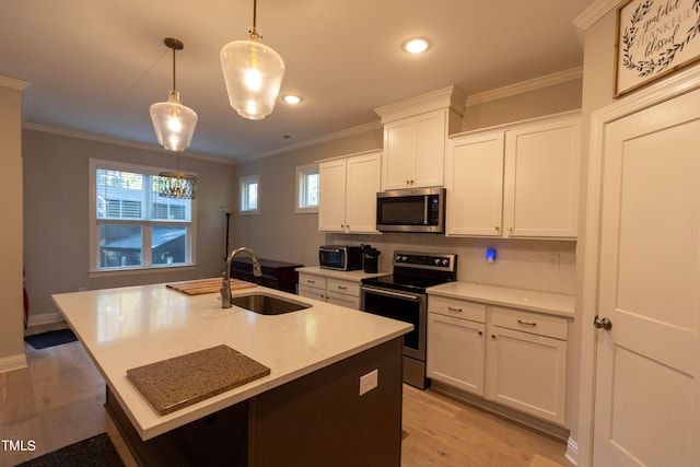 kitchen with stainless steel appliances, a center island with sink, sink, decorative light fixtures, and white cabinetry