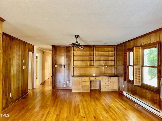 unfurnished living room featuring built in desk, light wood-type flooring, a baseboard radiator, built in shelves, and ceiling fan