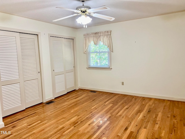 unfurnished bedroom with multiple closets, light hardwood / wood-style flooring, a textured ceiling, and ceiling fan