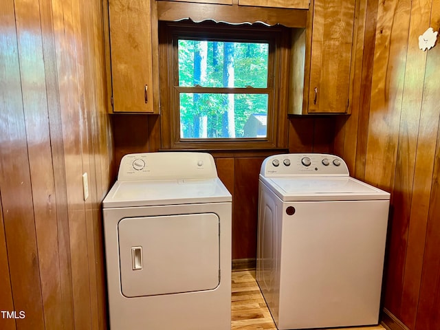 clothes washing area with wood walls, washing machine and clothes dryer, light hardwood / wood-style floors, and cabinets