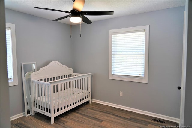 bedroom featuring ceiling fan, a nursery area, a textured ceiling, and dark wood-type flooring