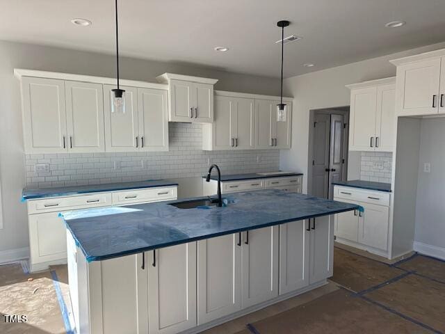 kitchen with hanging light fixtures, a kitchen island with sink, sink, and white cabinetry