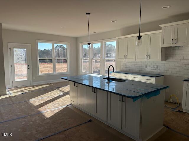 kitchen featuring pendant lighting, dark stone countertops, decorative backsplash, sink, and a kitchen island with sink