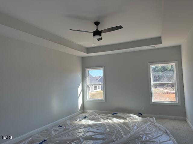 unfurnished bedroom with ceiling fan, carpet, and a raised ceiling