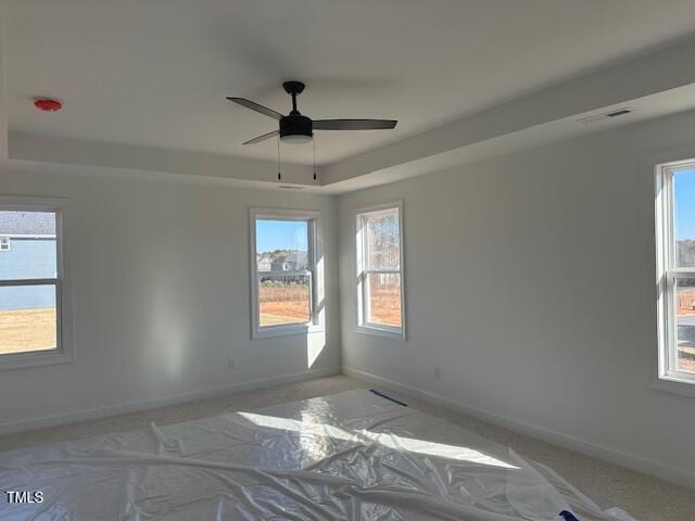 spare room with ceiling fan, a tray ceiling, carpet floors, and a healthy amount of sunlight