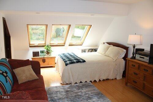 bedroom with a skylight, beamed ceiling, and light hardwood / wood-style flooring