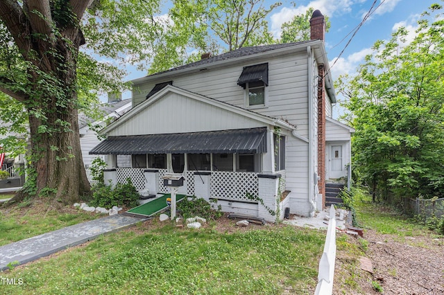 view of front of home with a sunroom, a chimney, and a front yard