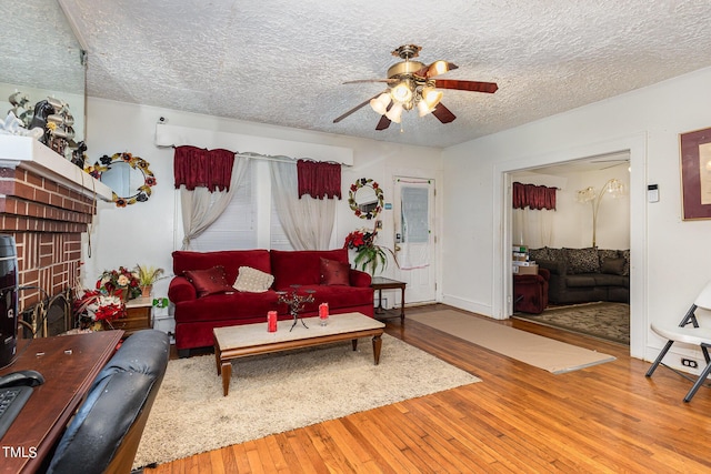 living area featuring a brick fireplace, a textured ceiling, ceiling fan, and hardwood / wood-style floors