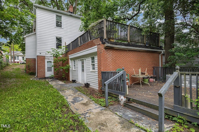 back of property with a chimney, a wooden deck, brick siding, a balcony, and a yard