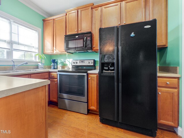 kitchen featuring light hardwood / wood-style floors, ornamental molding, black appliances, and sink