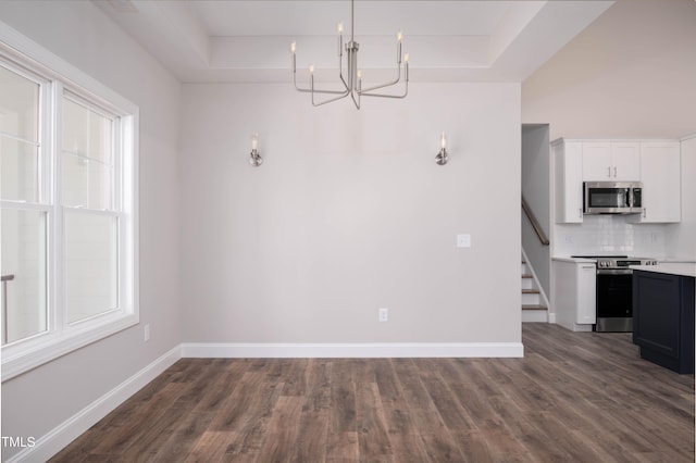 unfurnished dining area with dark wood-type flooring, a chandelier, and a raised ceiling