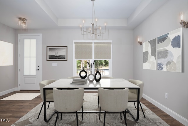 dining room with an inviting chandelier, a raised ceiling, and dark hardwood / wood-style flooring