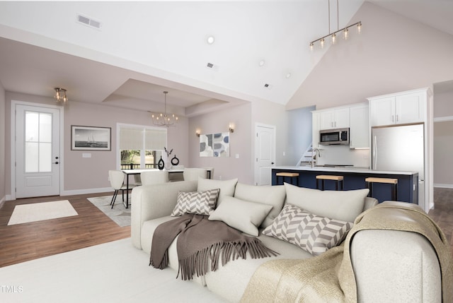 living room with sink, high vaulted ceiling, a notable chandelier, and light hardwood / wood-style flooring