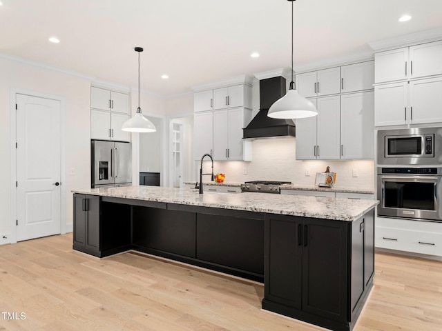 kitchen featuring appliances with stainless steel finishes, custom exhaust hood, a center island with sink, decorative light fixtures, and white cabinets