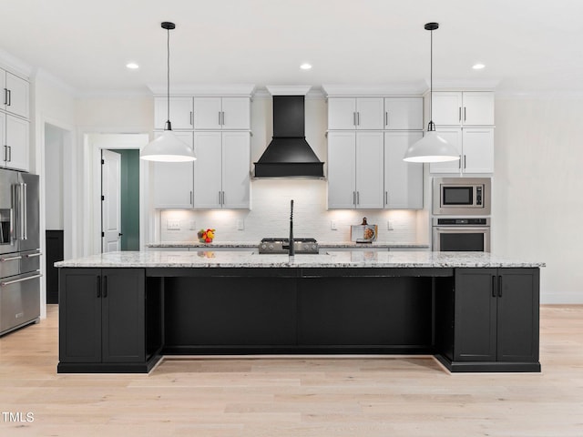 kitchen with appliances with stainless steel finishes, hanging light fixtures, premium range hood, and a large island with sink