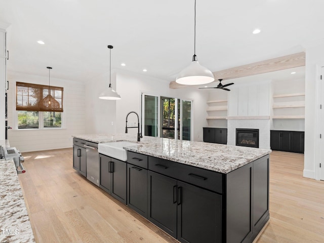 kitchen featuring decorative light fixtures, ceiling fan, sink, and an island with sink