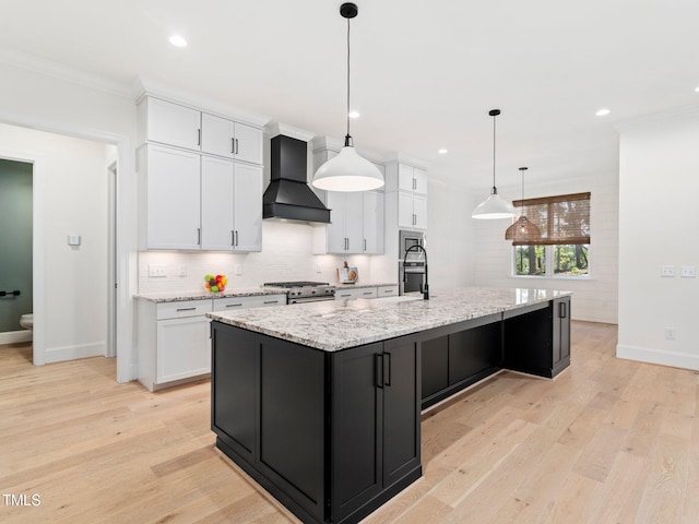 kitchen with light hardwood / wood-style floors, white cabinetry, custom range hood, and a kitchen island with sink