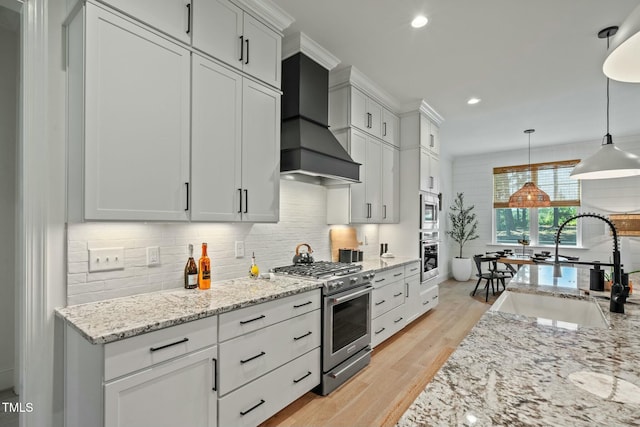 kitchen featuring tasteful backsplash, wall chimney exhaust hood, light wood-style flooring, appliances with stainless steel finishes, and a sink