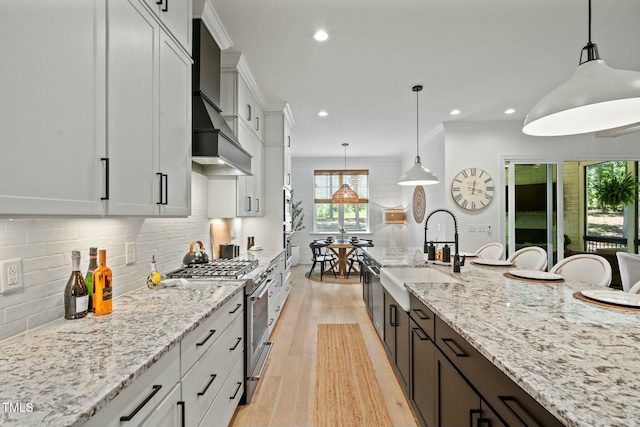 kitchen featuring a sink, light wood-style floors, wall chimney range hood, decorative backsplash, and stainless steel range