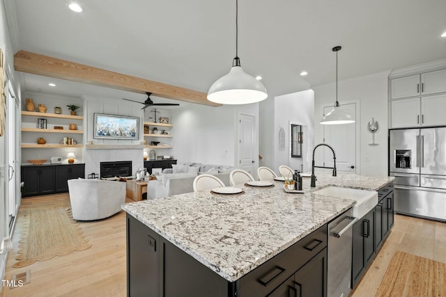 kitchen featuring light wood-style flooring, stainless steel appliances, a sink, an island with sink, and a glass covered fireplace